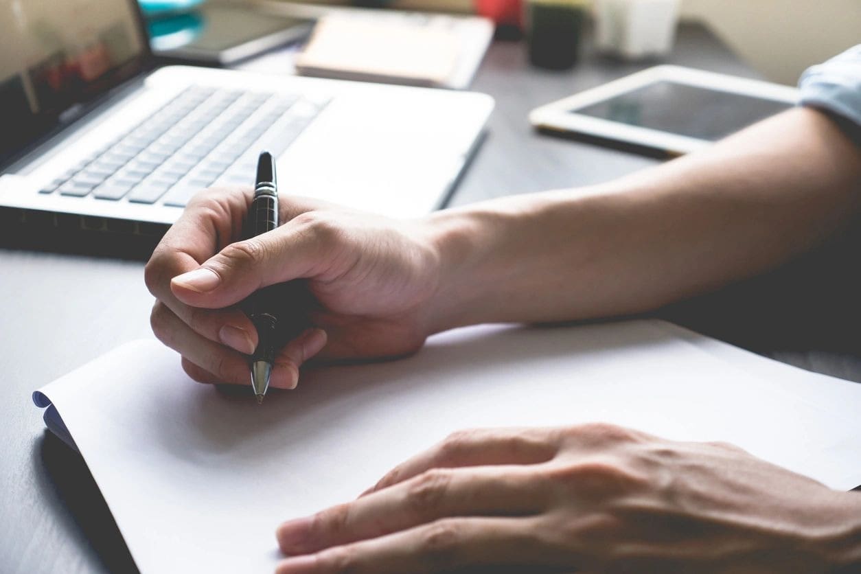 A person writing on paper with a pen.